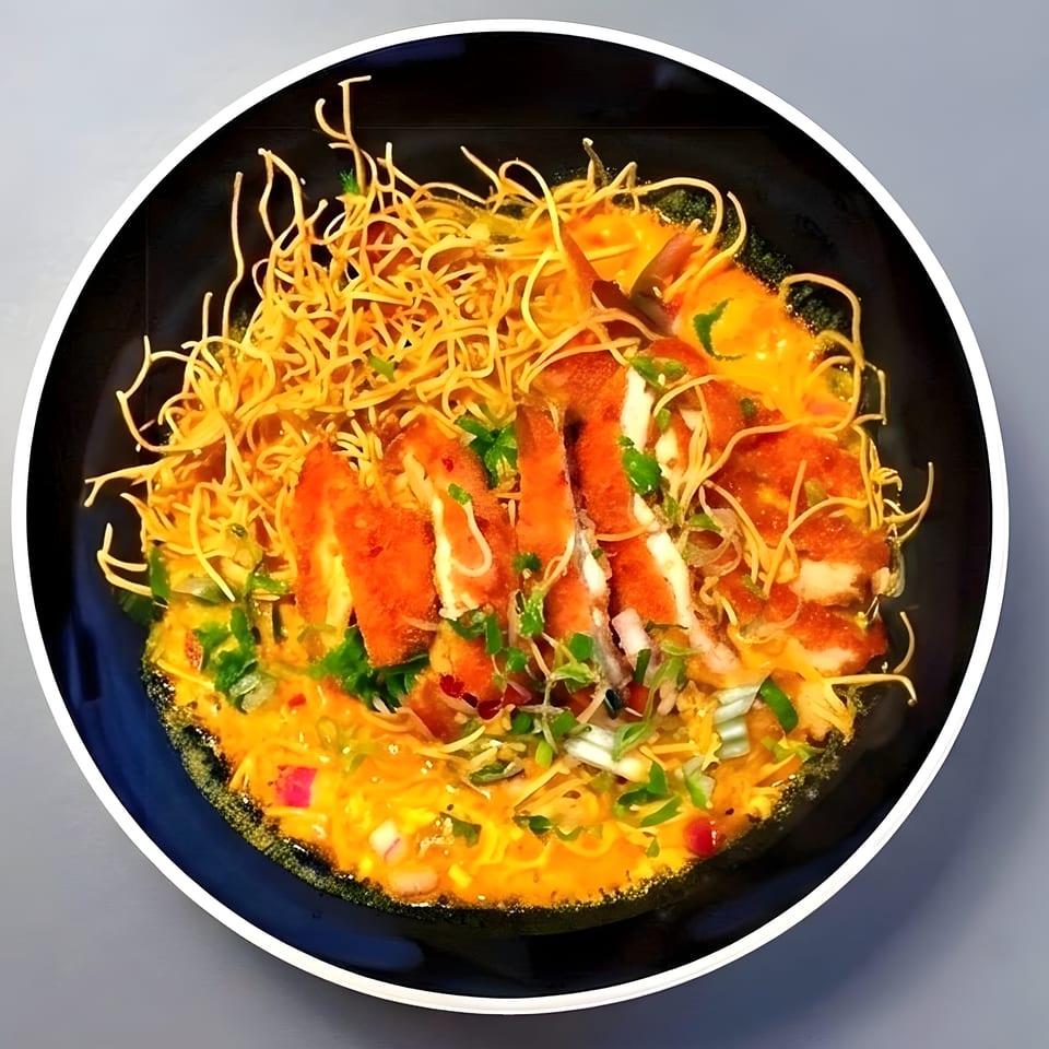 Crispy chicken slices and thin noodles in a rich yellow curry sauce, garnished with herbs.