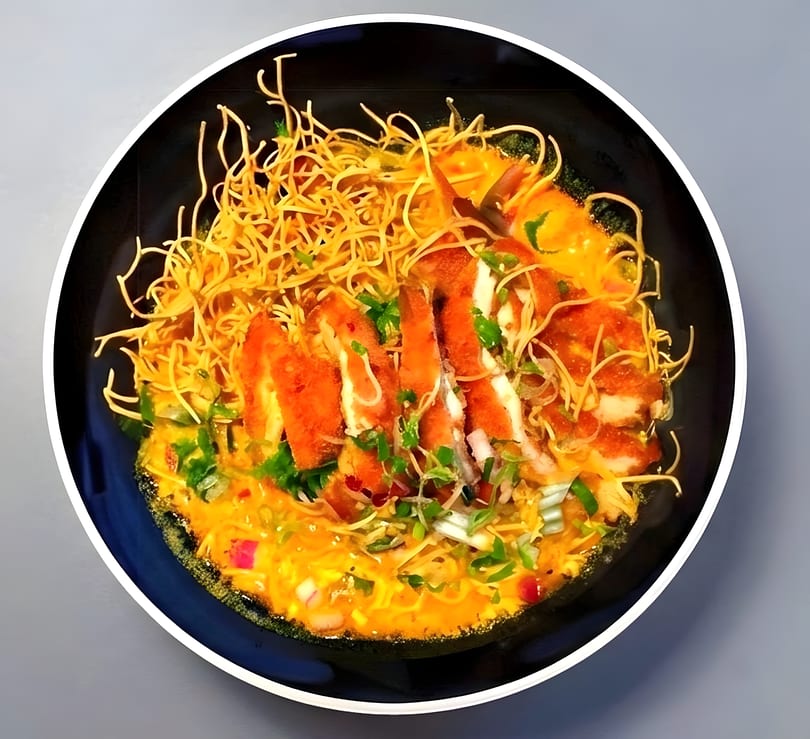 Crispy chicken slices and thin noodles in a rich yellow curry sauce, garnished with herbs.