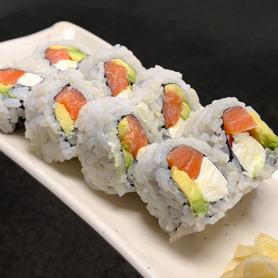 Six sushi rolls with salmon, avocado, and cream cheese on a white rectangular plate.