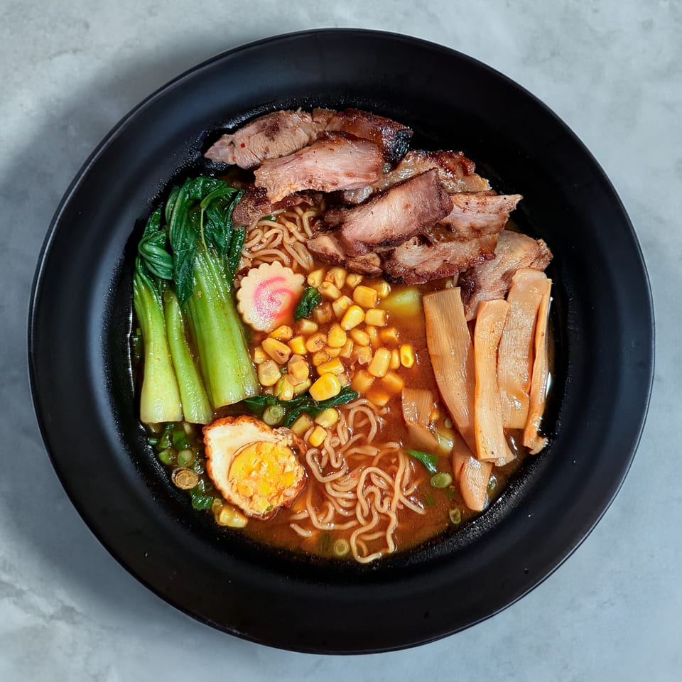 A black bowl of ramen with pork, bok choy, corn, bamboo shoots, and a soft-boiled egg.