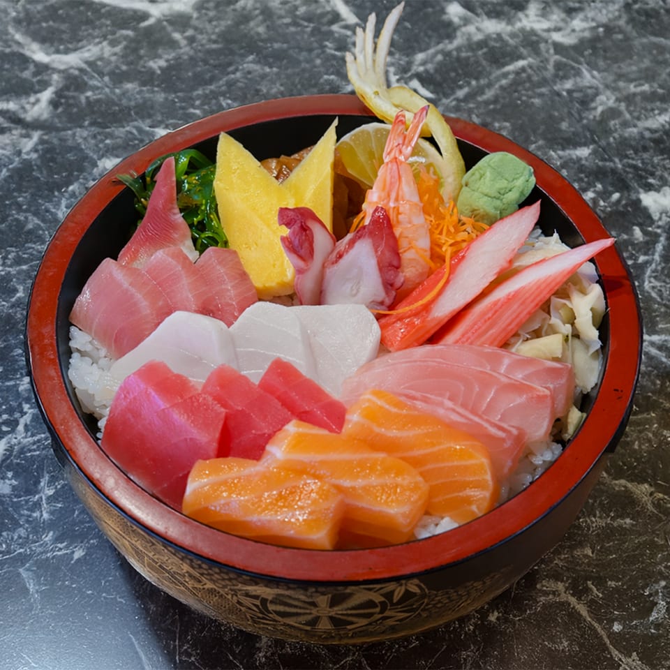 Colorful chirashi bowl with various sashimi, shrimp, crab, and egg over rice on a marble table.