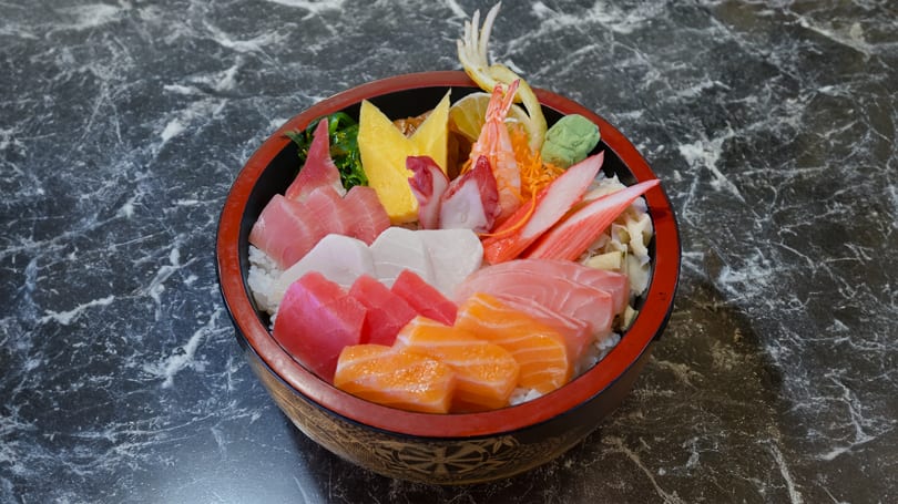 Colorful chirashi bowl with various sashimi, shrimp, crab, and egg over rice on a marble table.