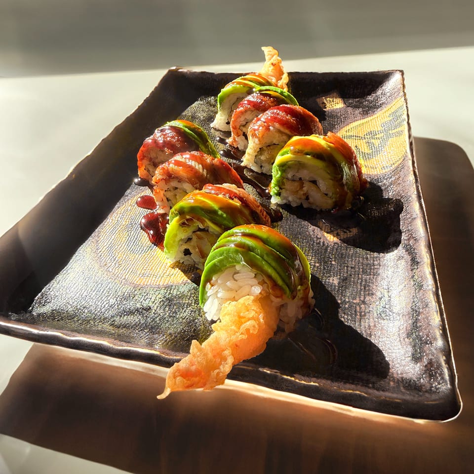 Dragon roll sushi with avocado, eel, and tempura shrimp on a dark, textured plate.