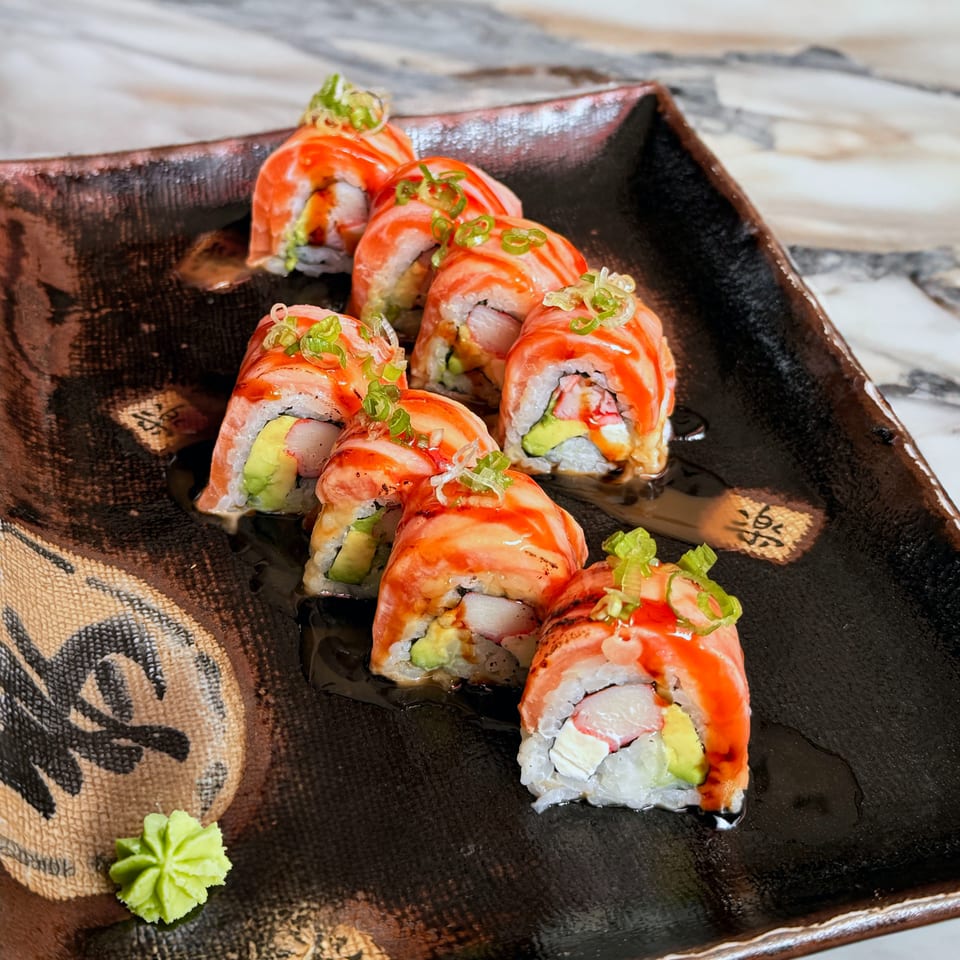 Salmon sushi rolls with avocado, crab, and cream cheese, drizzled with sauce and topped with scallions.