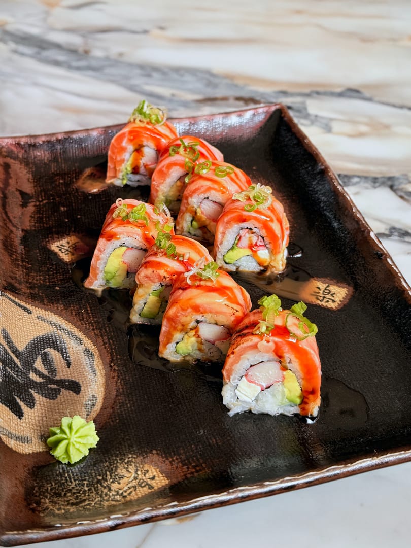 Salmon sushi rolls with avocado, crab, and cream cheese, drizzled with sauce and topped with scallions.